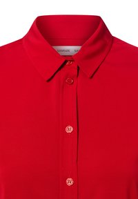 Rød skjorte med krage laget av glatt stoff, med dekorative knapper foran og en ren, strukturert nakke.