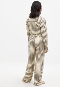 Striped two-piece outfit in beige and brown. Shirt features long sleeves and button closure, while pants have an elastic waistband and wide legs.