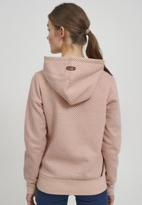 Sudadera de color rosa con un patrón de puntos, capucha con cordón, puños acanalados y una etiqueta de logo sutil en la parte posterior. Textura de tela suave.