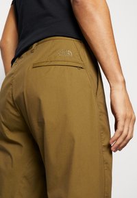 Kaki outdoor kalhoty s hladkou texturou, obsahující zadní kapsu na zip a vyšívané logo na pasu.