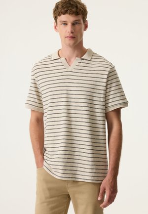 Beige kurzärmliges Polohemd mit marineblauen horizontalen Streifen; V-Ausschnitt mit strukturiertem Stoff; lockere Passform. Kombiniert mit hellen Hosen.