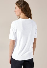 T-shirt bianco a maniche corte con vestibilità rilassata, scollatura rotonda e texture morbida, mostrato da dietro su uno sfondo neutro.
