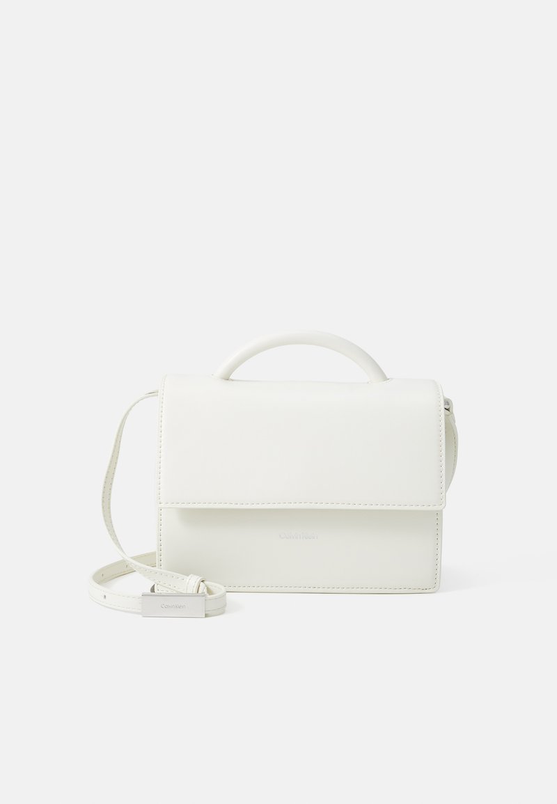 Sac à main en cuir blanc avec un design structuré, une anse supérieur, une bandoulière amovible et un rabat à l'avant. Présente un branding subtil et une texture lisse.