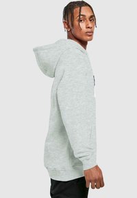 Sudadera gris claro hecha de tela suave, con un bolsillo frontal, puños acanalados y capucha con cordón. Presenta un pequeño logo en el pecho.