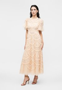 Γυναίκα με μπεζ midi φόρεμα από δαντέλα με φουσκωτά τούλινα μανίκια και floral σχέδια, συνδυασμένο με καφέ σανδάλια με ψηλό τακούνι.