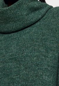 Grön stickad polotröja med ett mjukt, texturerat tyg, med en lös, draperad krage och en något tjock look.