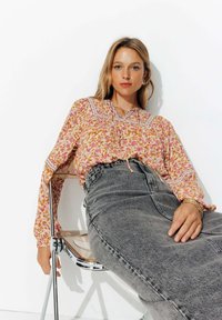 Blouse à motifs floraux dans des teintes de rose et d'orange avec un design plissé au niveau de l'encolure, associée à une jupe en denim gris à taille haute.
