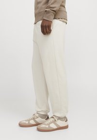 Cremefarvede sweatpants med elastiske manchetter, parret med beige sneakers med en struktureret sål og trekantede mønstre på overdelen.