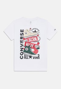 Camiseta de algodón blanca con un gráfico de cuatro zapatillas apiladas en beige, rojo y verde, con el texto "Converse All Star" y acentos de manzana.