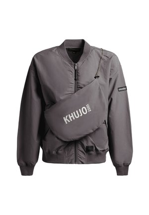 Giubbotto bomber grigio con zip, collo e polsini a coste, abbinato a una borsa a tracolla coordinata con il logo "KHUJO 2001" in bianco.