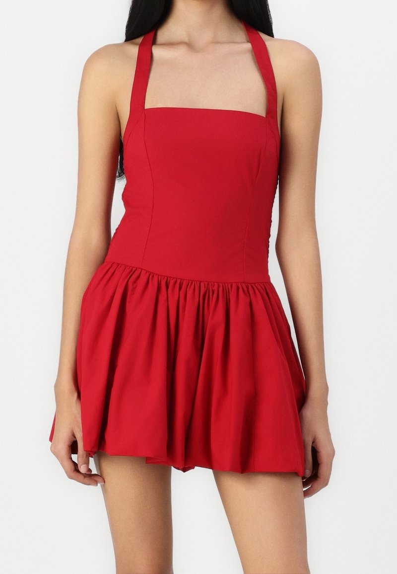 Robe rouge à bretelles avec un décolleté carré, un corsage ajusté et une jupe évasée. Tissu en coton lisse avec une texture froncée à la taille.