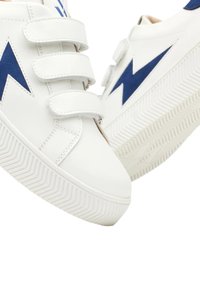 Scarpa bianca con design a fulmine blu, dotata di tre cinturini in velcro e suola in gomma testurizzata con un motivo a zigzag.