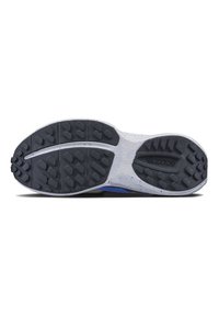 Shoe outsole features a textured black rubber surface with multidirectional lugs for grip, set against a white flexible midsole.