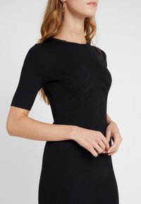 Abito in maglia nera a costine con maniche corte, silhouette aderente e dettagli a motivo foglia sul corpo. Tessuto liscio e design che abbraccia il corpo.
