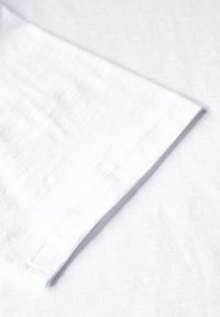 Tessuto di lino bianco e leggero con una texture liscia. Presenta un semplice orlo a manica arrotolata con dettagli di cucitura visibili.