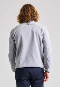 Giacca in fleece grigia chiara con colletto alto, tasca laterale con zip e logo nero sul retro, caratterizzata da una texture morbida e una vestibilità comoda.