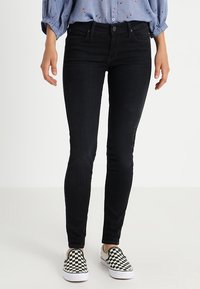 Jeans ajustados negros, con una textura suave, diseño tradicional de cinco bolsillos y cintura de altura media, combinados con unos zapatos de cuadros en blanco y negro.
