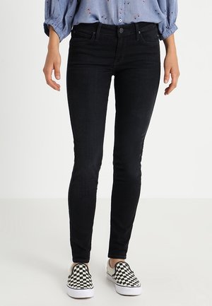 Jeans ajustados negros, con una textura suave, diseño tradicional de cinco bolsillos y cintura de altura media, combinados con unos zapatos de cuadros en blanco y negro.