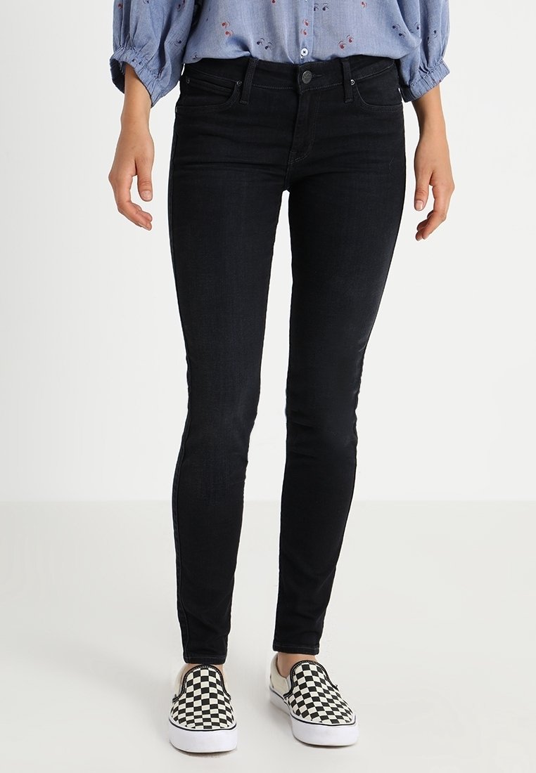 Jeans ajustados negros, con una textura suave, diseño tradicional de cinco bolsillos y cintura de altura media, combinados con unos zapatos de cuadros en blanco y negro.