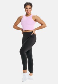 Roosa lühike sportlik tank top, mustad kõrge vöökohtadega retuusid ja valged spordijalatsid. Sile kangas minimaalse õmbluse detaili ja logoga aktsentidega.