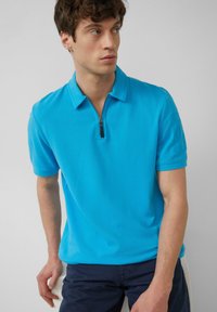 Koszulka polo z krótkim rękawem w kolorze turkusowym z zamkiem błyskawicznym w kołnierzyku, wykonana z gładkiego materiału; charakteryzuje się subtelnym logo na rękawie.