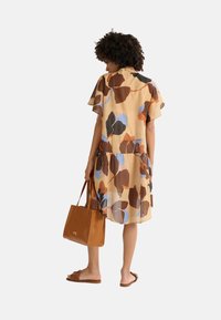 Robe à motifs floraux bruns et bleus avec des manches à volants, un ourlet en étages, assortie à un sac à main beige et des sandales marron.
