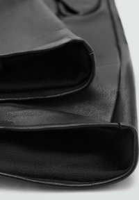 Tejido de cuero negro que muestra una superficie suave con una ligera textura, doblada en los bordes, creando un aspecto limpio y minimalista.