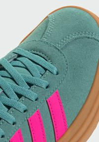 Sneaker con tomaia in suede verde acqua, strisce testurizzate rosa e lacci azzurri chiari. Presenta una suola in gomma beige e dettagli di cucitura a contrasto.