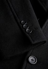 Czarny wełniany płaszcz o miękkiej fakturze, z dopasowanym kołnierzem i czterema okrągłymi czarnymi guzikami na przednim listwie.