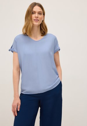 Blouse bleu clair à manches courtes avec un décolleté en V et des détails de manches nouées, fabriquée en tissu doux, assortie à un pantalon large marine.