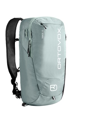 Person trägt einen grün karierten Rucksack mit gesicherten schwarzen Gurten über einer dunkel bordeauxfarbenen Jacke.