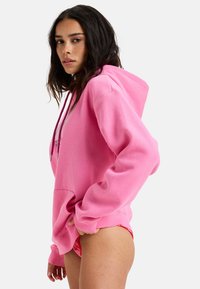 Rosa huvtröja i mjukt tyg med en rymlig känguruficka, justerbara dragkedjor och ribbade muddar. Lite oversized passform.