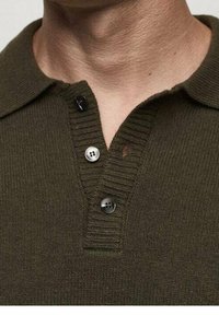 Polo en tricot vert olive foncé avec un col côtelé, trois boutons et un petit détail en trou près des boutons.