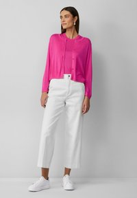 Gilet rose en tricot porté sur un haut assorti, associé à un pantalon large blanc et des baskets blanches. Conception simple, texture douce.