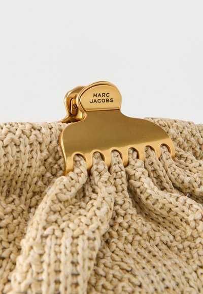 Κούμπωμα σε χρυσό τόνο με εγχάραξη "MARC JACOBS" που στερεώνει μπεζ υφαντό ύφασμα με χοντρή πλεκτή υφή.