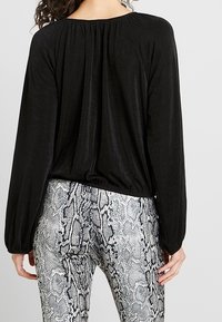 Czarna bluzka z długim rękawem, zebranym dekoltem i luźnym krojem, w połączeniu z dopasowanymi szarymi legginsami w wężowy wzór z fakturowanymi detalami.