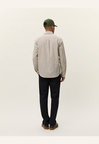 Langermet skjorte med knapper i beige med rutemønster, vist fra bak. Kombinert med mørke bukser og en grønn caps.