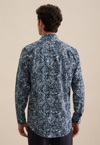 Camicia a maniche lunghe realizzata in un morbido tessuto con una base blu scuro, caratterizzata da intricati motivi paisley in blu chiaro e bianco. Polsini con bottoni.