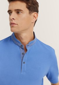 Kurzarm-Polohemd aus einfarbigem blauen Baumwollstoff mit stehendem Kragen, blauer Kontraststoff am Kragen und drei schwarzen Knöpfen.