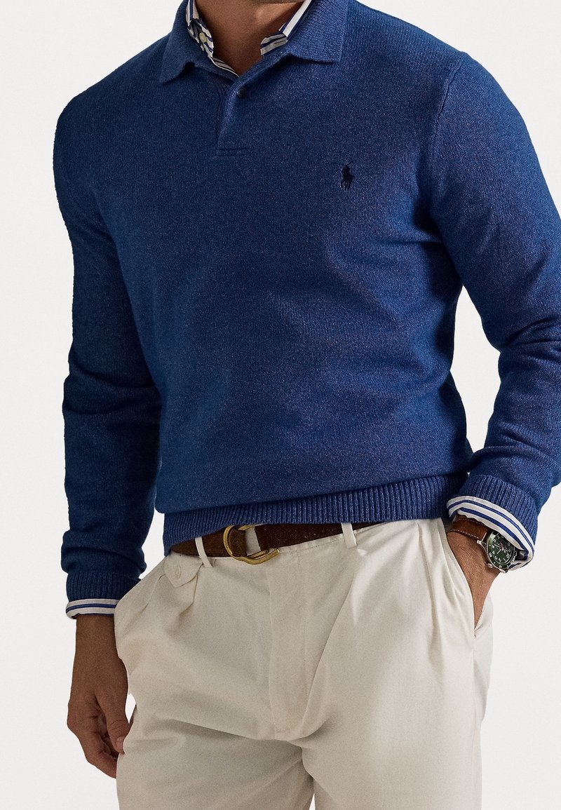 Tumma sininen neulepusero, jossa on poolokaulus, ribbaus hihoissa ja helmassa. Rinnassa pieni logo. Yhdistetty vaalean kermanvärisiin housuihin.