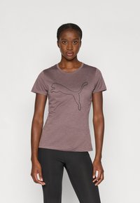 Fioletowy t-shirt z krótkim rękawem wykonany z miękkiego materiału, z czarnym logo Pumy na środku. Noszony z czarnymi legginsami.