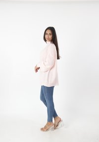Maglione a costine rosa chiaro con collo alto, abbinato a jeans skinny blu e sandali con tacco trasparente, mostrato di lato.