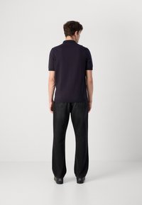 Ναυτικό πόλο μπλούζα με κοντό μανίκι, από βαμβακερό υλικό, επίπεδο πλεκτό γιακά. Μαύρα παντελόνια φαρδιάς γραμμής με λεία υφή. Μαύρα παπούτσια.