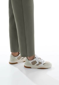 Sneaker bianche e beige con accenti testurizzati, design con lacci e suole in gomma. Indossate con pantaloni larghi di colore verde oliva.