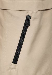 Tissu beige avec une fermeture éclair noire verticale. La fermeture éclair possède une tirette texturée et un design épuré et minimal. Les coutures sont visibles le long des bords.