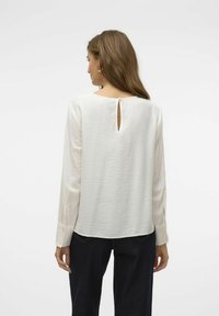 Blusa chiara in crema con maniche lunghe, scollatura rotonda, dettaglio a chiave sulla schiena e polsini con bottoni. Tessuto testurizzato con finitura liscia.