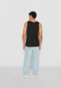 Black sleeveless tank top paired with light blue wide-leg jeans. The fabric appears smooth, with a relaxed fit and minimal stitching details.