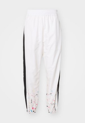 Witte trainingsbroek met zwarte zijstrepen en veelkleurige verfspatten nabij elastische enkelboorden.