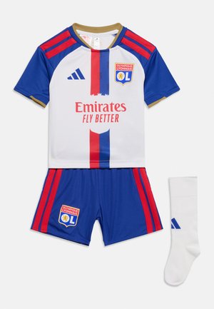 Λευκή και μπλε στολή ποδοσφαίρου του Olympique Lyonnais με κόκκινες ρίγες, λογότυπο χορηγού Emirates και λευκές κάλτσες με μπλε λογότυπο Adidas.