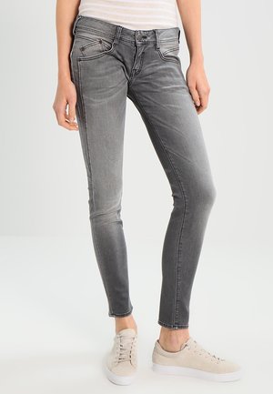 Jeans grigi slim-fit con una finitura sbiadita, dotati di cinque tasche e dettagli di cuciture a contrasto. Abbinati a scarpe da ginnastica beige chiaro.